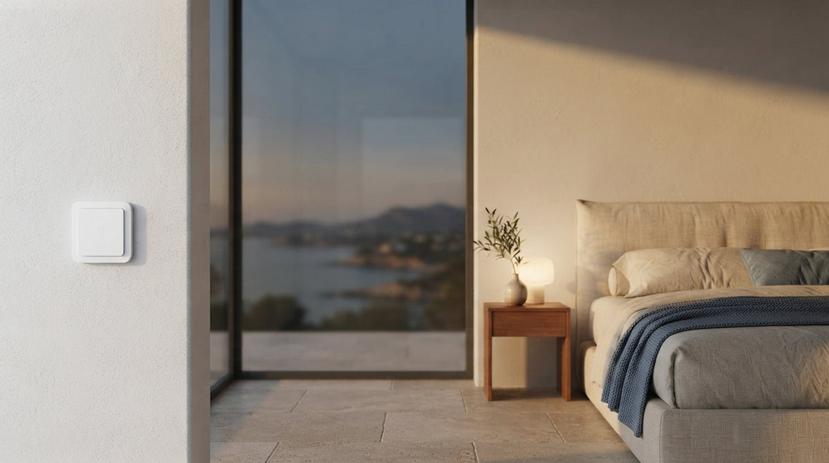 Modern bedroom interior with a smart light switch on the wall and a view of the Spanish coast at sunset.
